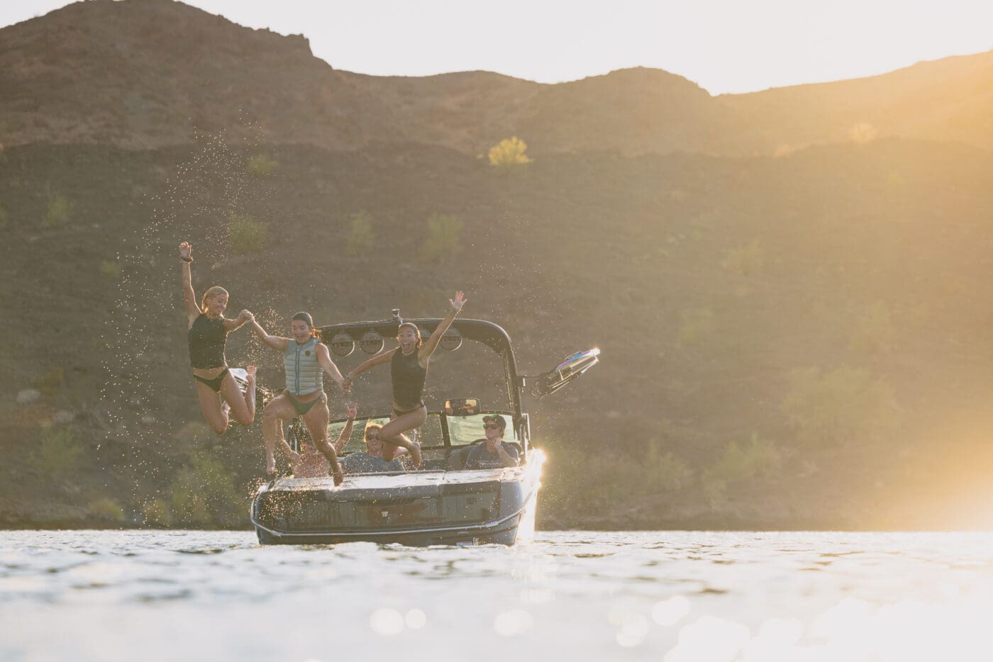 A group of girls jump into the lake off of a MasterCraft wake boat.