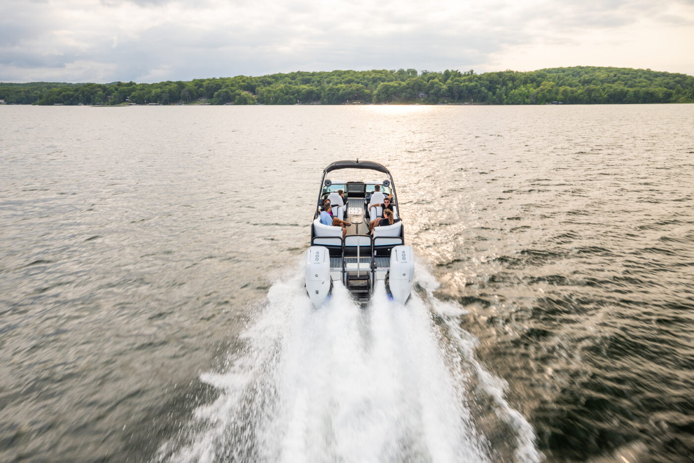 A twin engine ponton riding across the water at sunset.